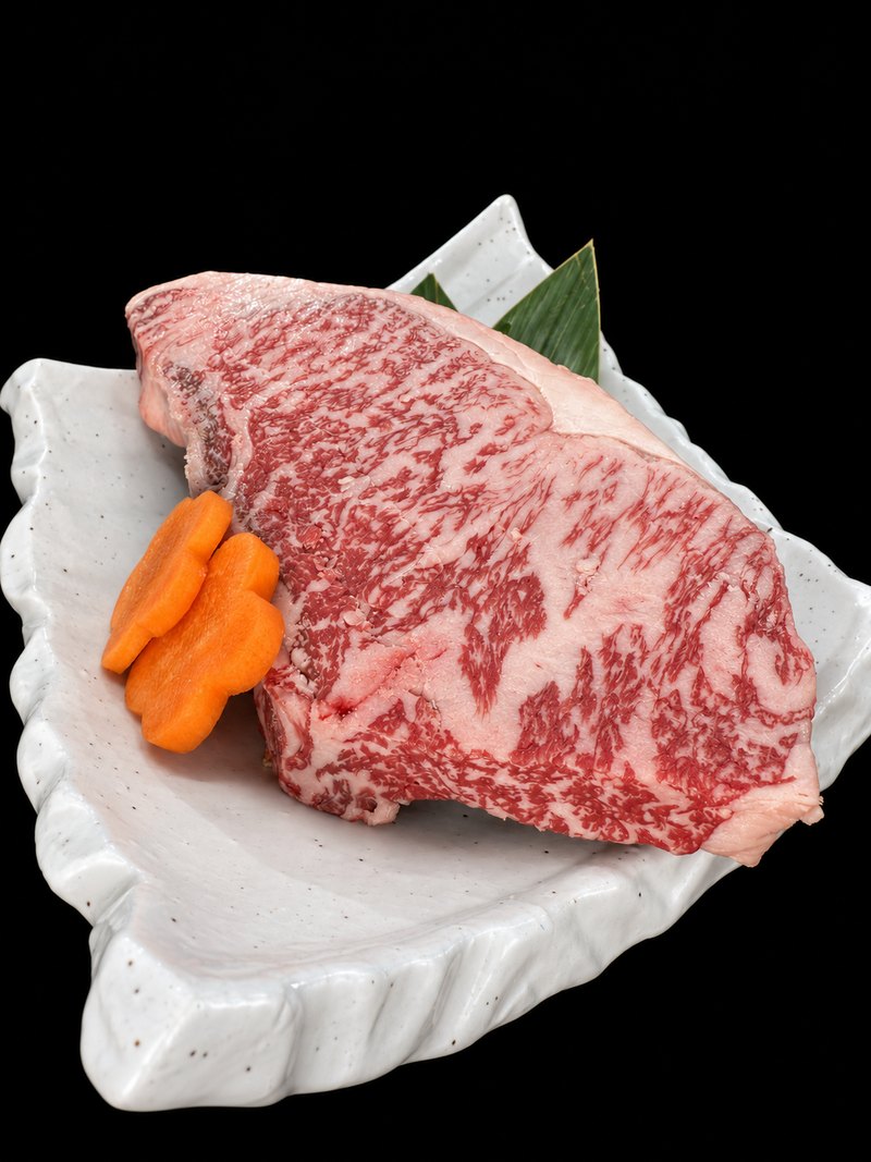 白い皿に載せた、細やかな霜降りと白い脂の縁がある厚切りの肉