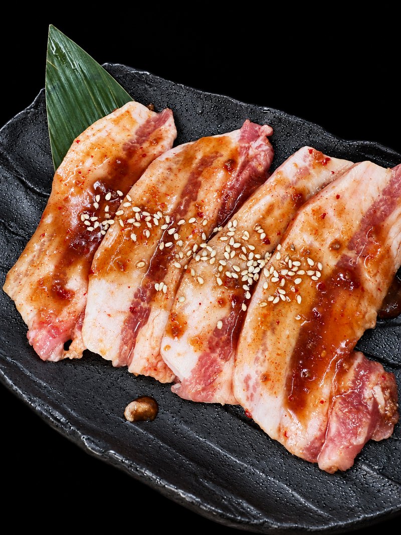 黒い皿に、たれをからめ白ごまを振った厚みのある肉を並べた一皿