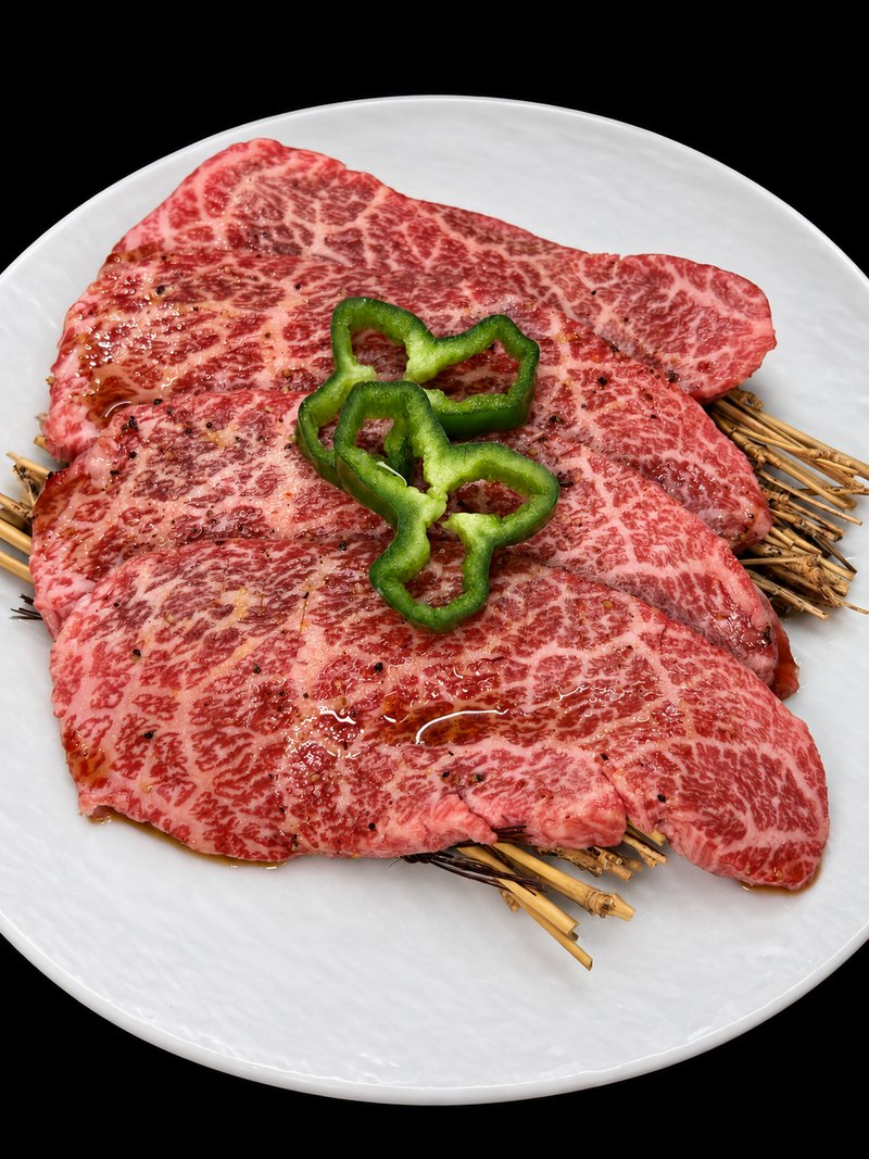 白い丸皿に、たれをまとった薄切りの肉を広げ、ピーマンの輪切りを添えた一皿