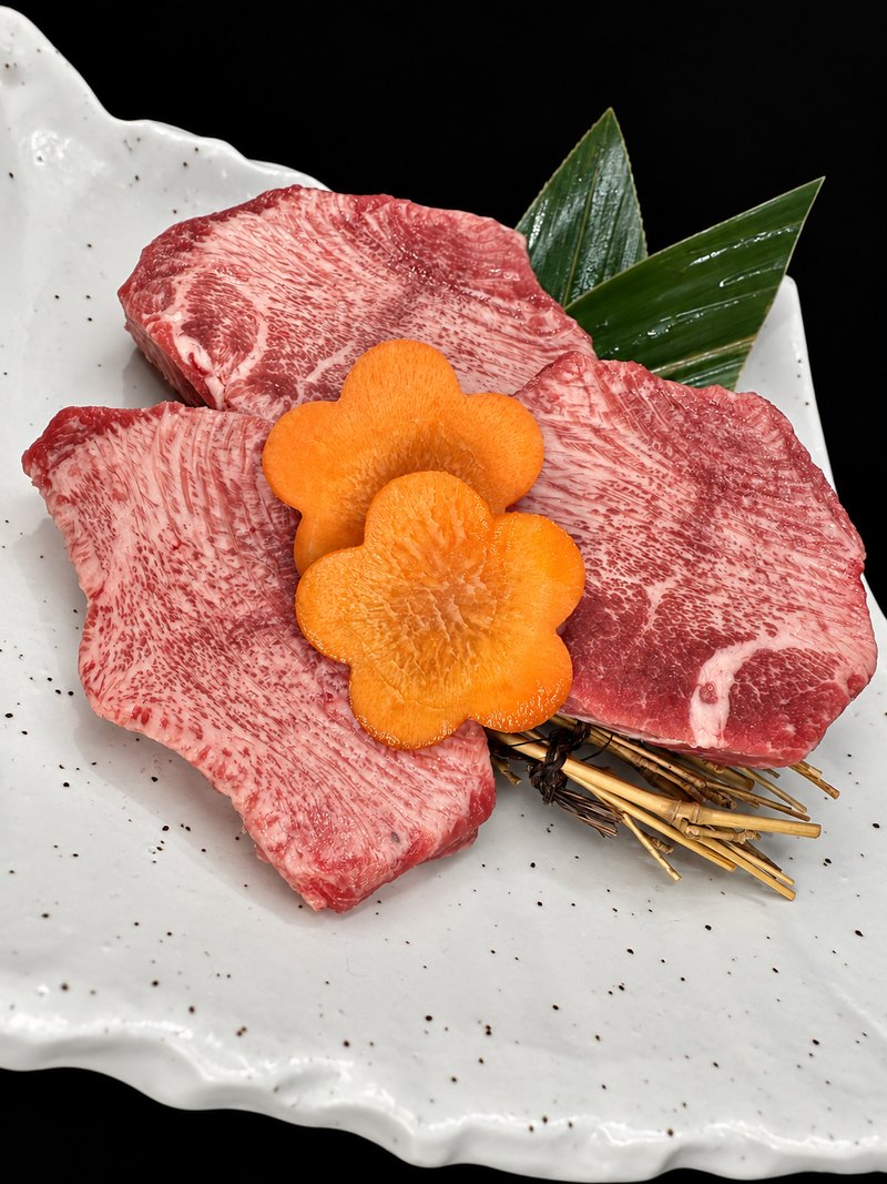 白い角皿に、大きめに切り分けた霜降りの肉を広げ、にんじんの飾り切りを添えた一皿