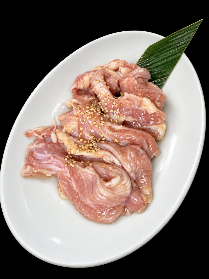 白い楕円皿に、細く切った淡い色の肉を盛り、ごまを振った一皿