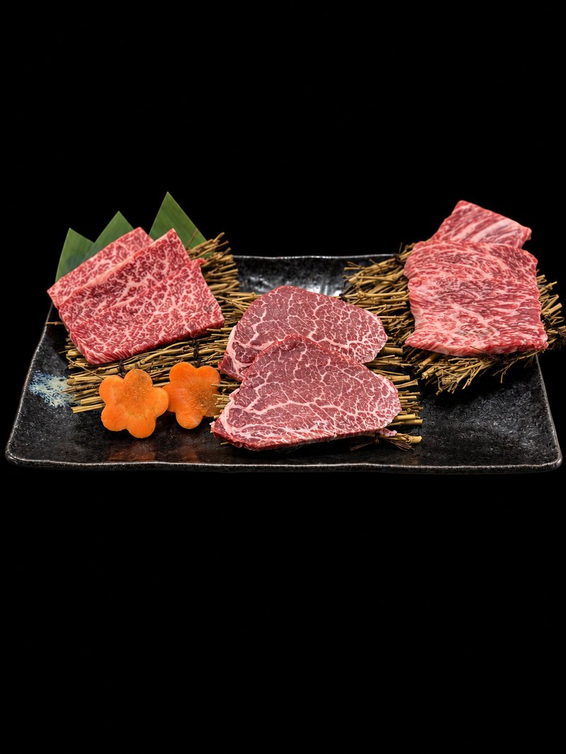 黒い角皿に、切り分けた肉を三種並べ、にんじんの飾り切りを添えた一皿