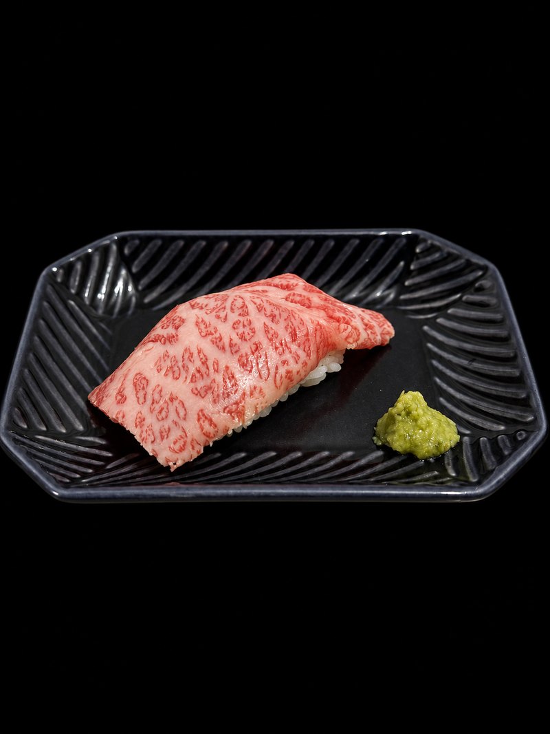 黒い角皿に盛られた、炙った霜降りの肉をのせた寿司とわさび