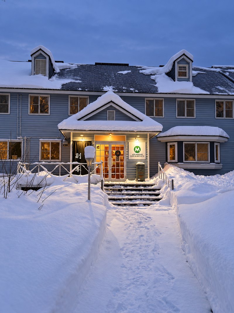 夕暮れの青い空の下、屋根に雪を積もらせた建物と、除雪された雪道の先にある入口